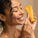 Smiling woman under the shower holding a yellow tube: the signature gel wash. With water and bubbles on her skin.